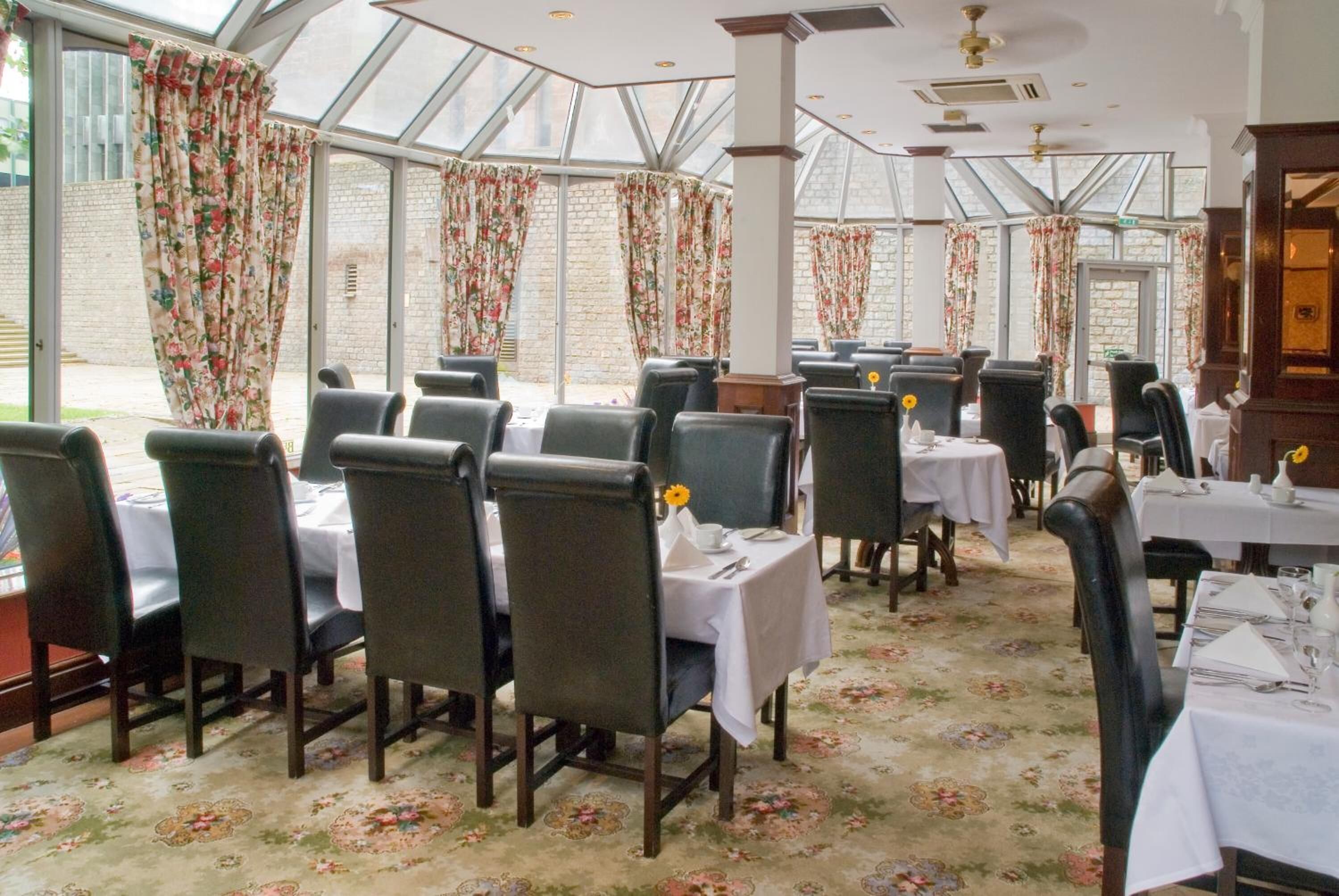 A restaurant with a glass roof, floral curtains, and tables set for dining.
