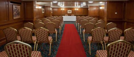 A conference room with rows of chairs, a red carpet, and wooden paneling.