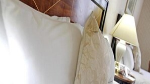 Una cama bien hecha con sábanas blancas y una almohada decorativa.