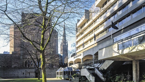 Un patio con un árbol, un edificio de varios pisos y una torre al fondo.