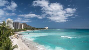 A beach with clear turquoise waters, palm trees, and a mountain in the background.