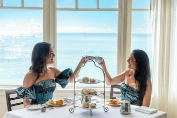 Two individuals in white robes standing by a window with a view of the beach. at Moana Surfrider, A Westin Resort & Spa, Waikiki Beach