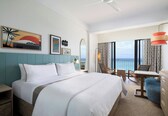 A hotel room with a large bed, a desk, a chair, and a view of the ocean.