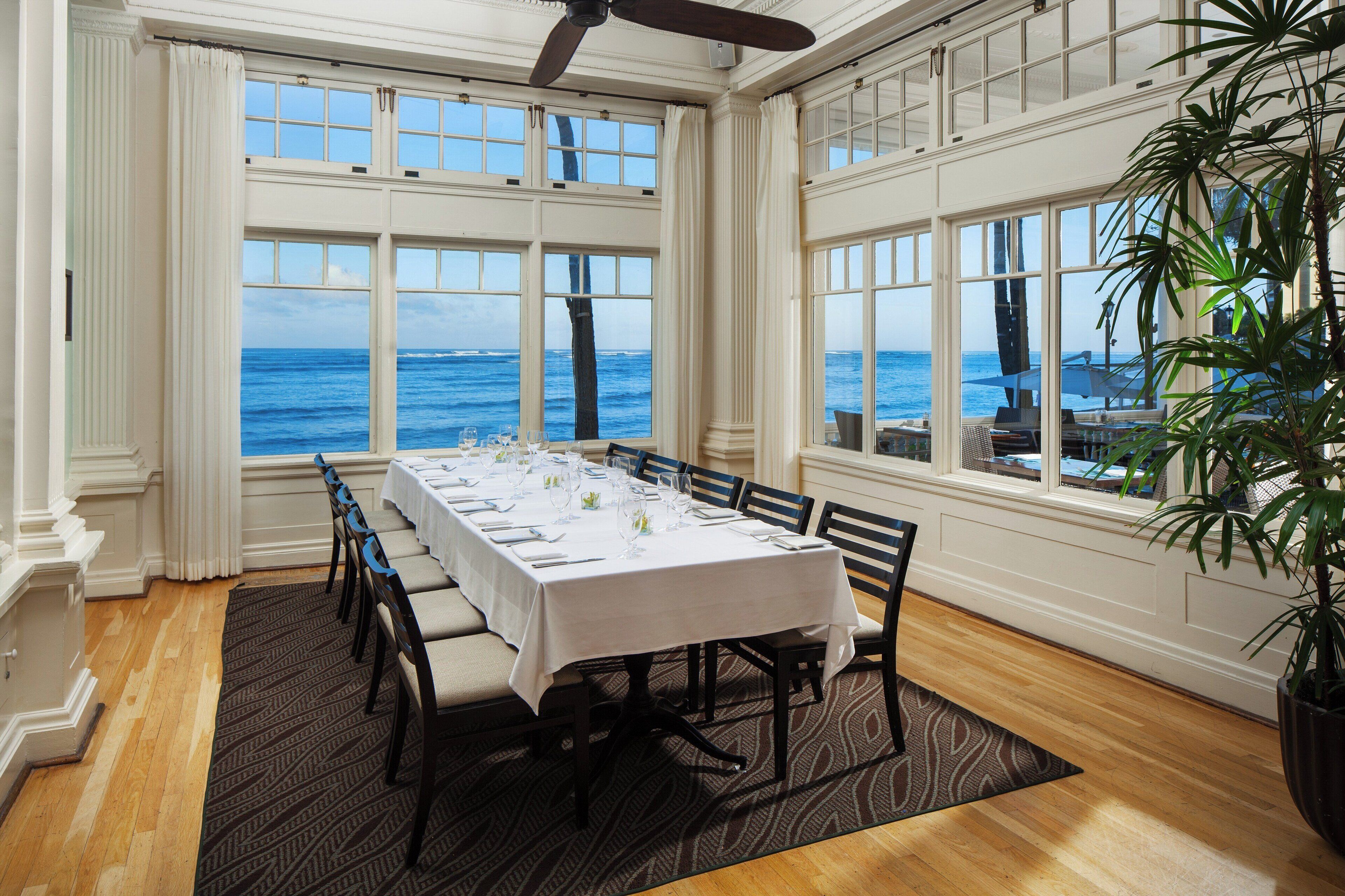 A dining room with a view of the ocean, a ceiling fan, and a potted plant.