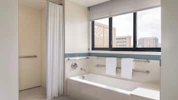 A modern bathroom with a bathtub, shower, and window.