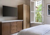 A bedroom with a bed, a wardrobe, a television, and a window with shutters.
