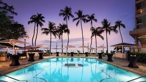 Ein Pool mit Liegestühlen und Sonnenschirmen, umgeben von Palmen, in einem Resort.
