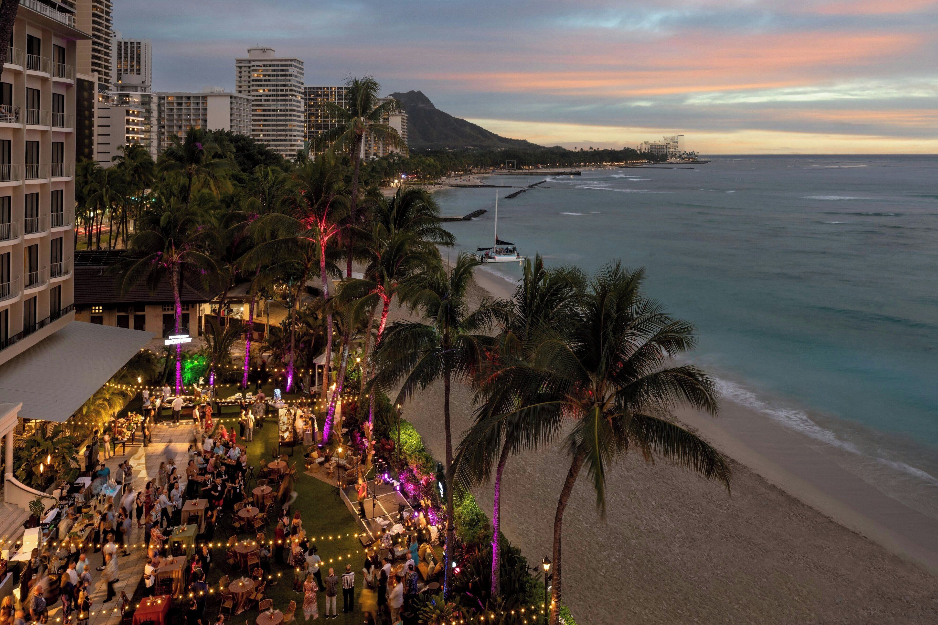 A rooftop bar with a view of the beach and ocean, surrounded by palm trees and hotel buildings.