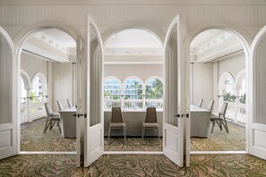 A room with a large table and chairs, arched doorways, and a view of palm trees through large windows.