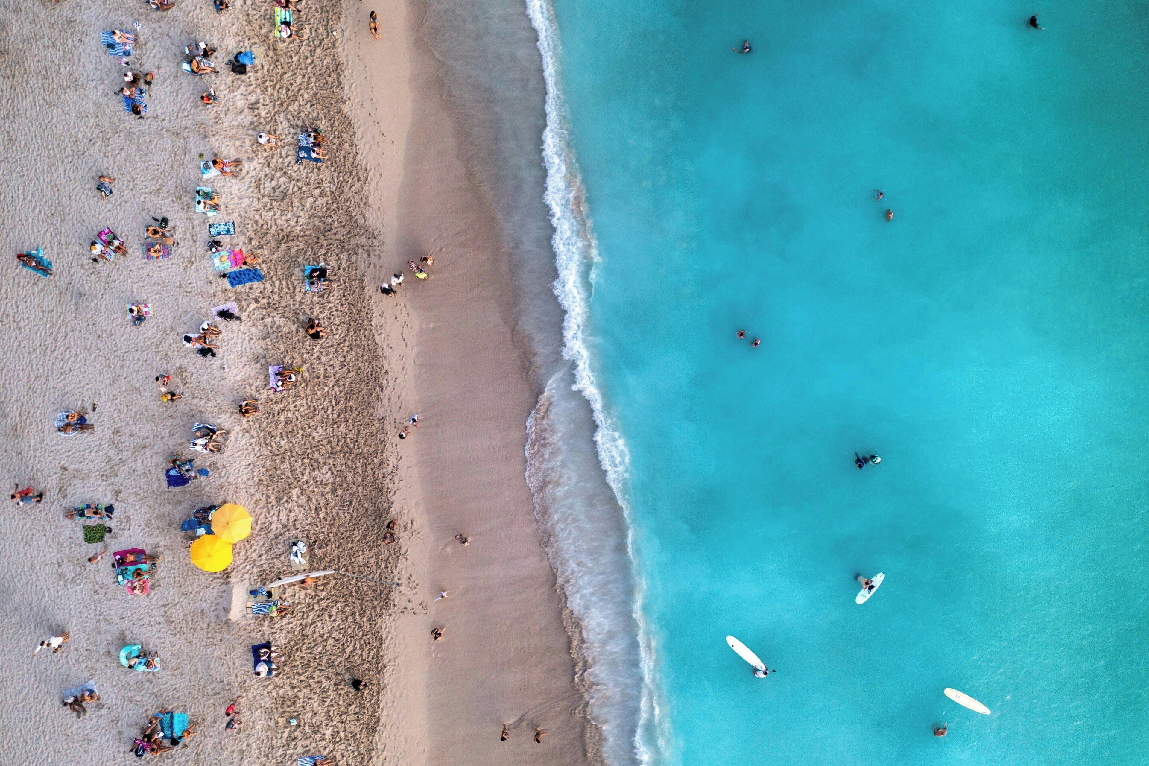 An aerial view of a beach with people, umbrellas, and surfboards.
