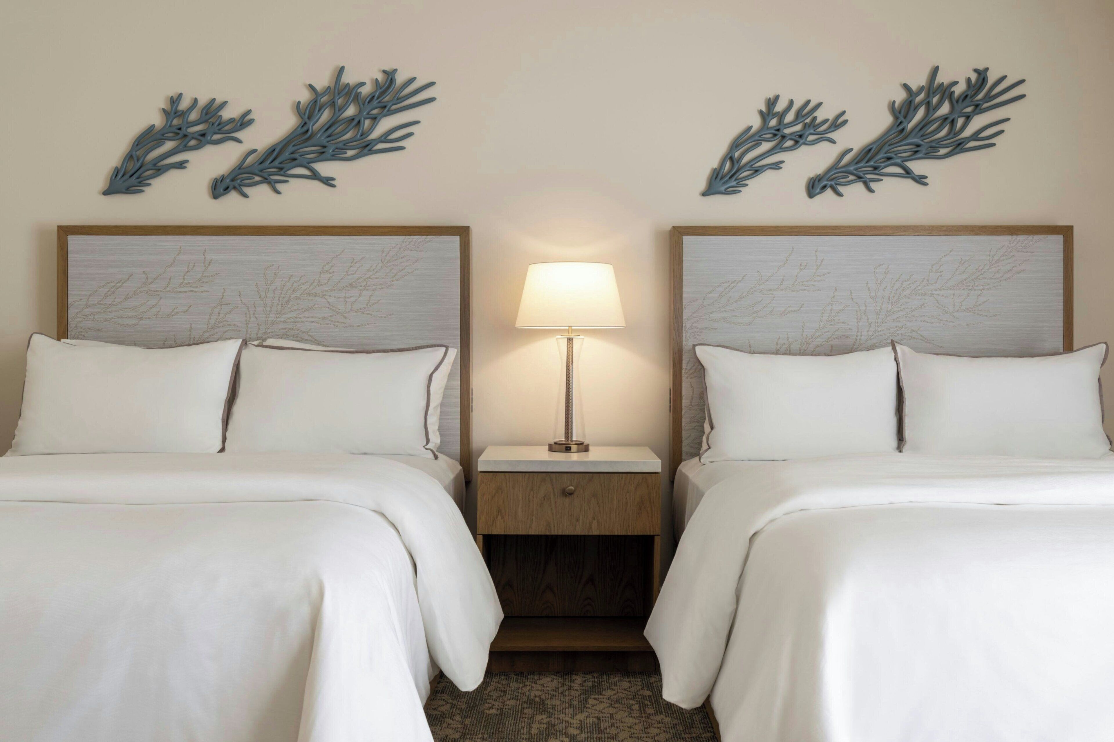 A hotel room with two beds, a nightstand with a lamp, and wall art.