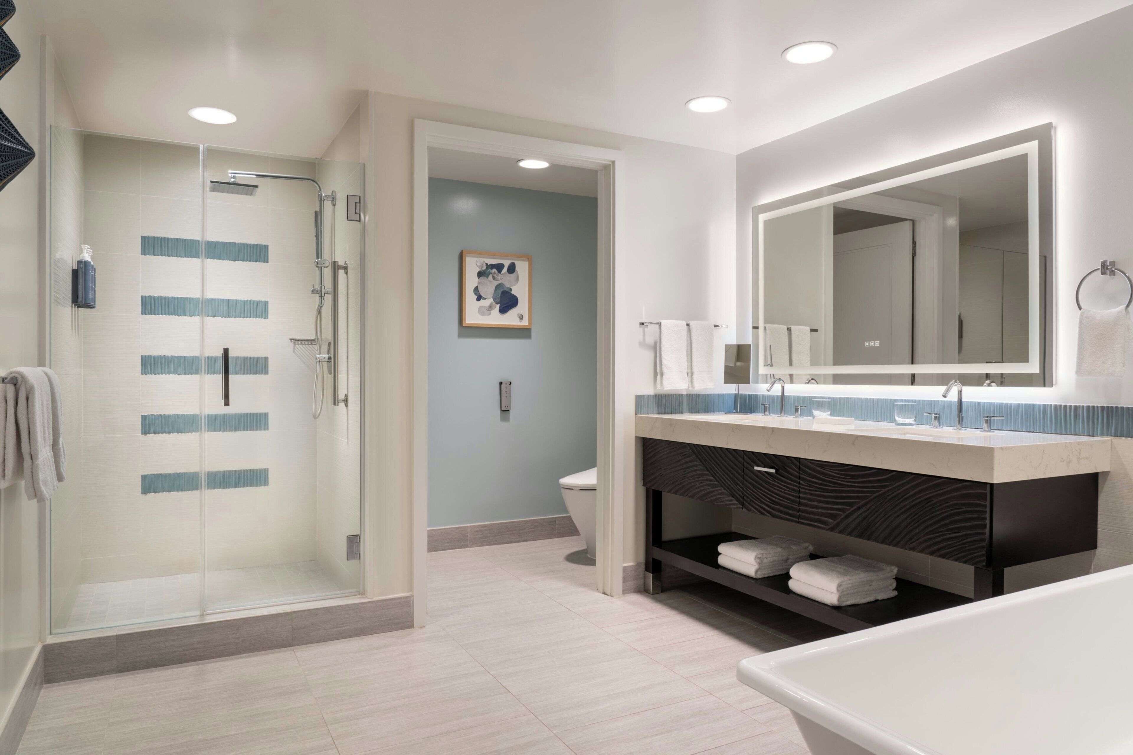 A modern bathroom with a glass shower enclosure, a large mirror, and a bathtub.