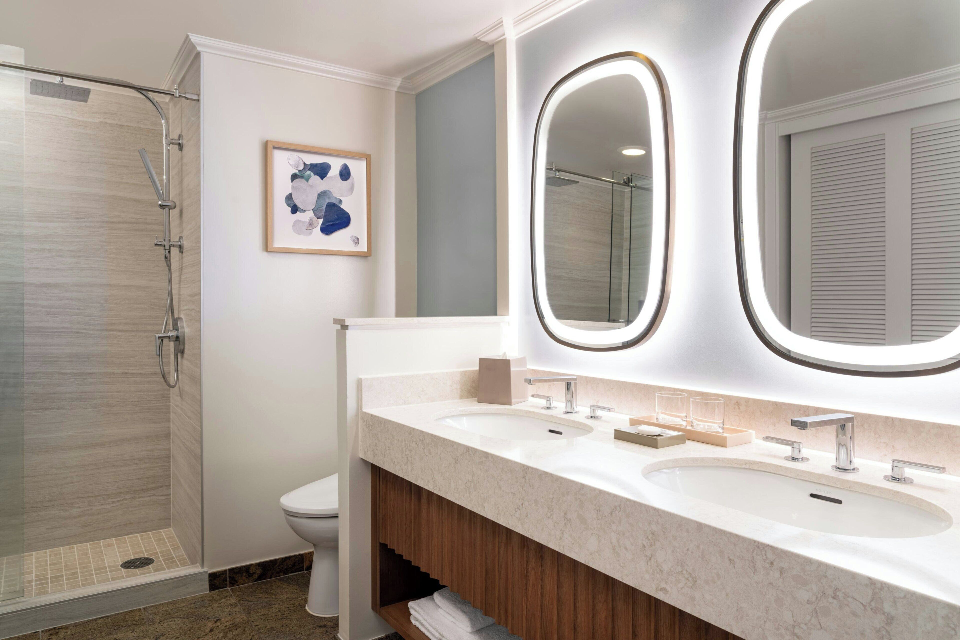 Un baño moderno con ducha acristalada, dos lavamanos y un espejo grande con iluminación integrada.