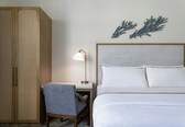 A hotel room with a bed, a desk with a chair, a lamp, and a wardrobe.