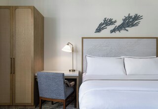 A hotel room with a bed, a desk with a chair, a lamp, and a wardrobe.