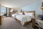A hotel room with two beds, a sofa, a small table, and a view of the ocean.