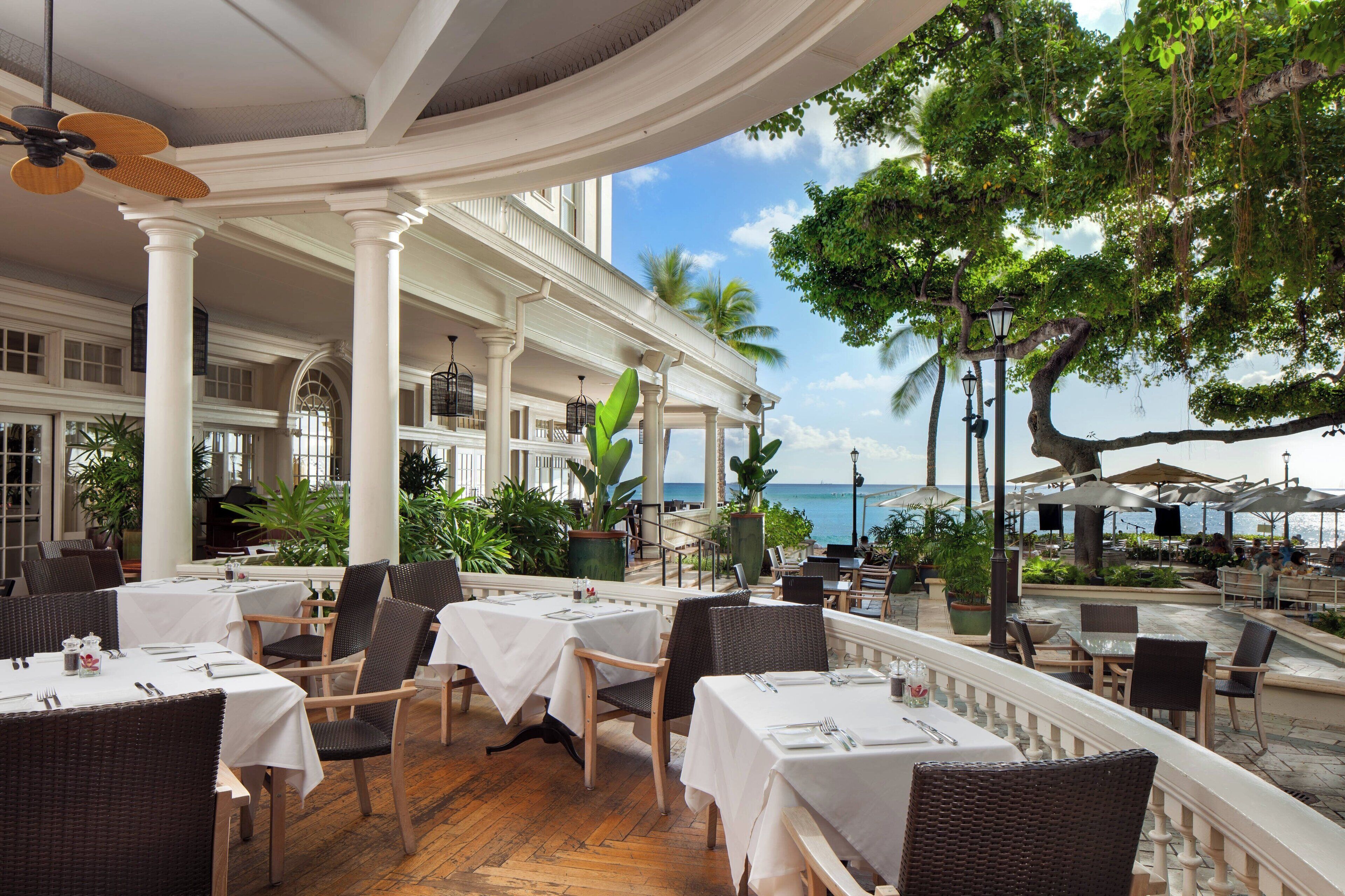 Ein Restaurant mit weißen Tischen und Stühlen, großen Fenstern und Blick auf das Meer.