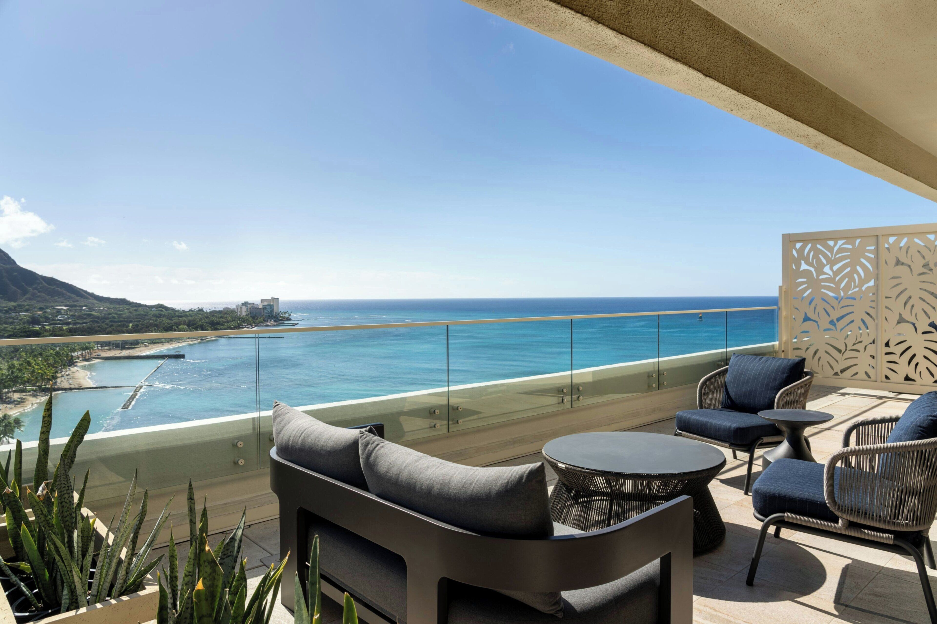 A balcony with outdoor furniture, a glass railing, and a view of the ocean and coastline.