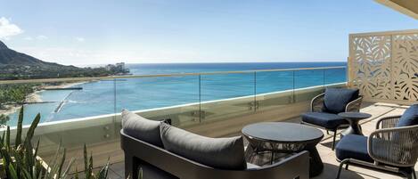 A balcony with outdoor furniture, a glass railing, and a view of the ocean and coastline.