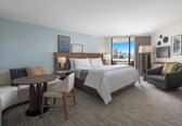 A hotel room with a bed, a desk, a chair, a sofa, and a view of the city.