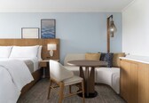 A hotel room with a bed, a chair, a small table, a sofa, and a lamp.