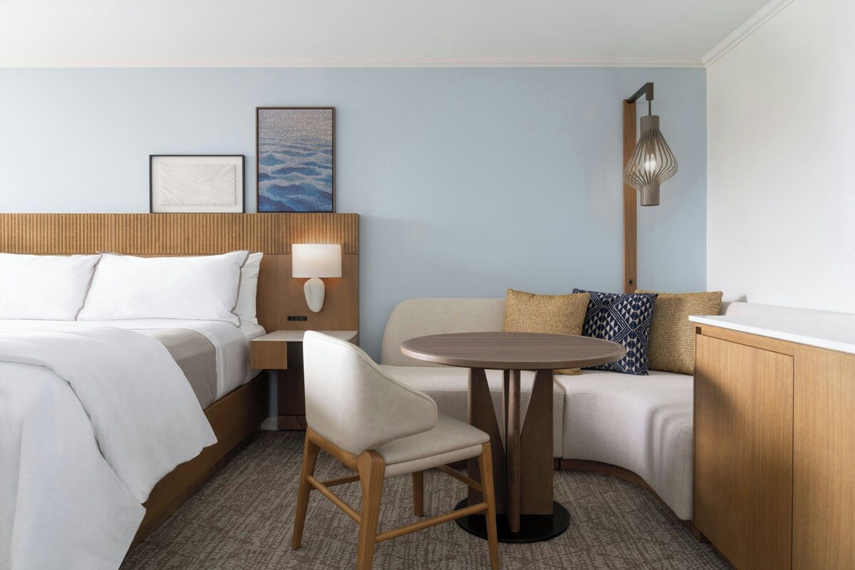 A hotel room with a bed, a chair, a small table, a sofa, and a lamp.