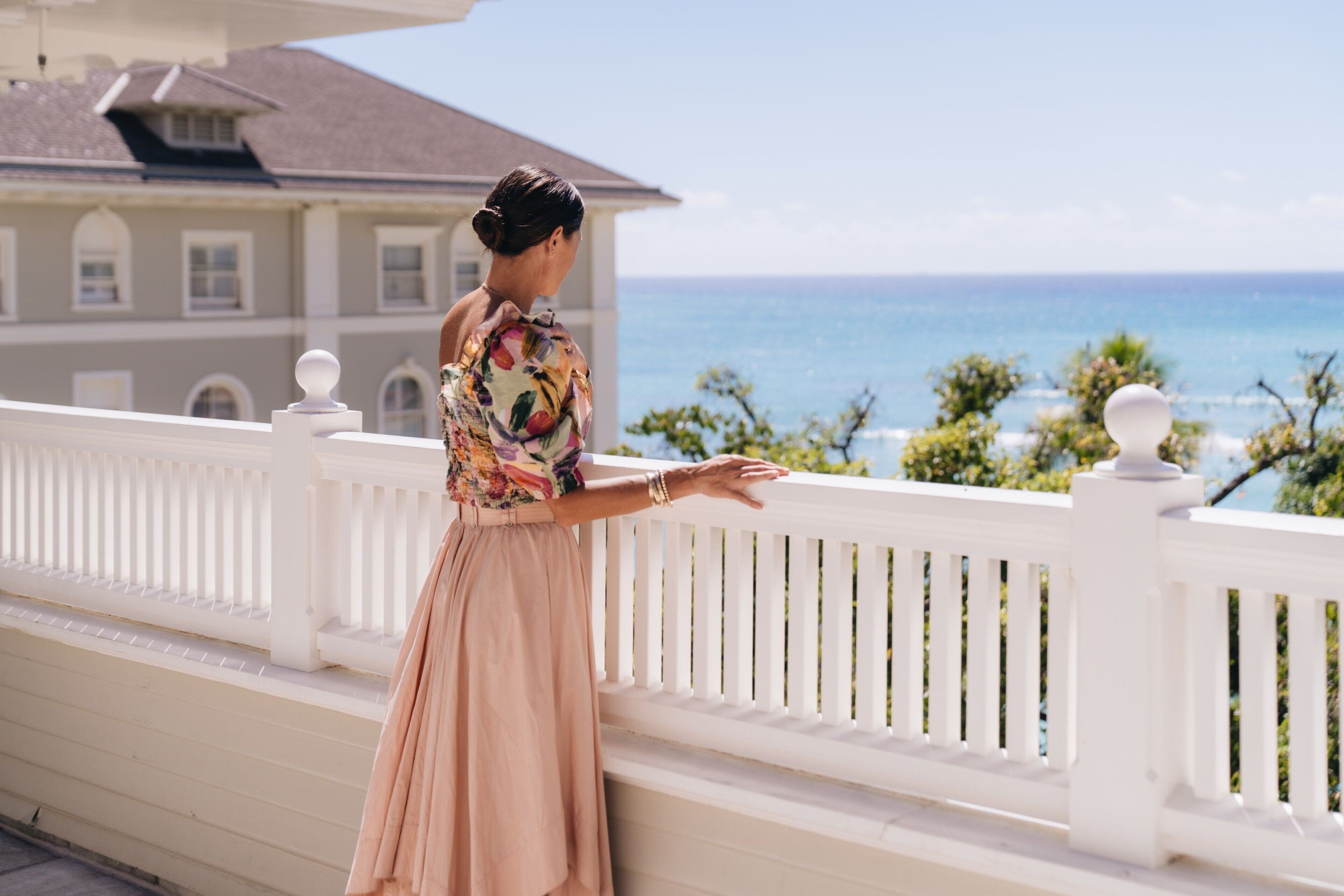 A person standing on a balcony with a view of the ocean and a building in the background.