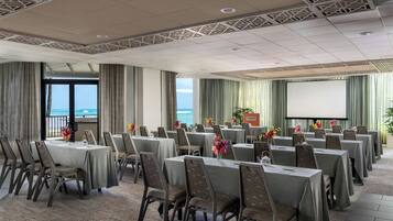 A conference room with tables and chairs, a projector screen, and a view of the ocean.