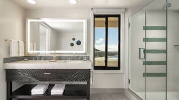 A modern bathroom with a large mirror, dual sinks, a dark patterned vanity, and a glass shower enclosure.