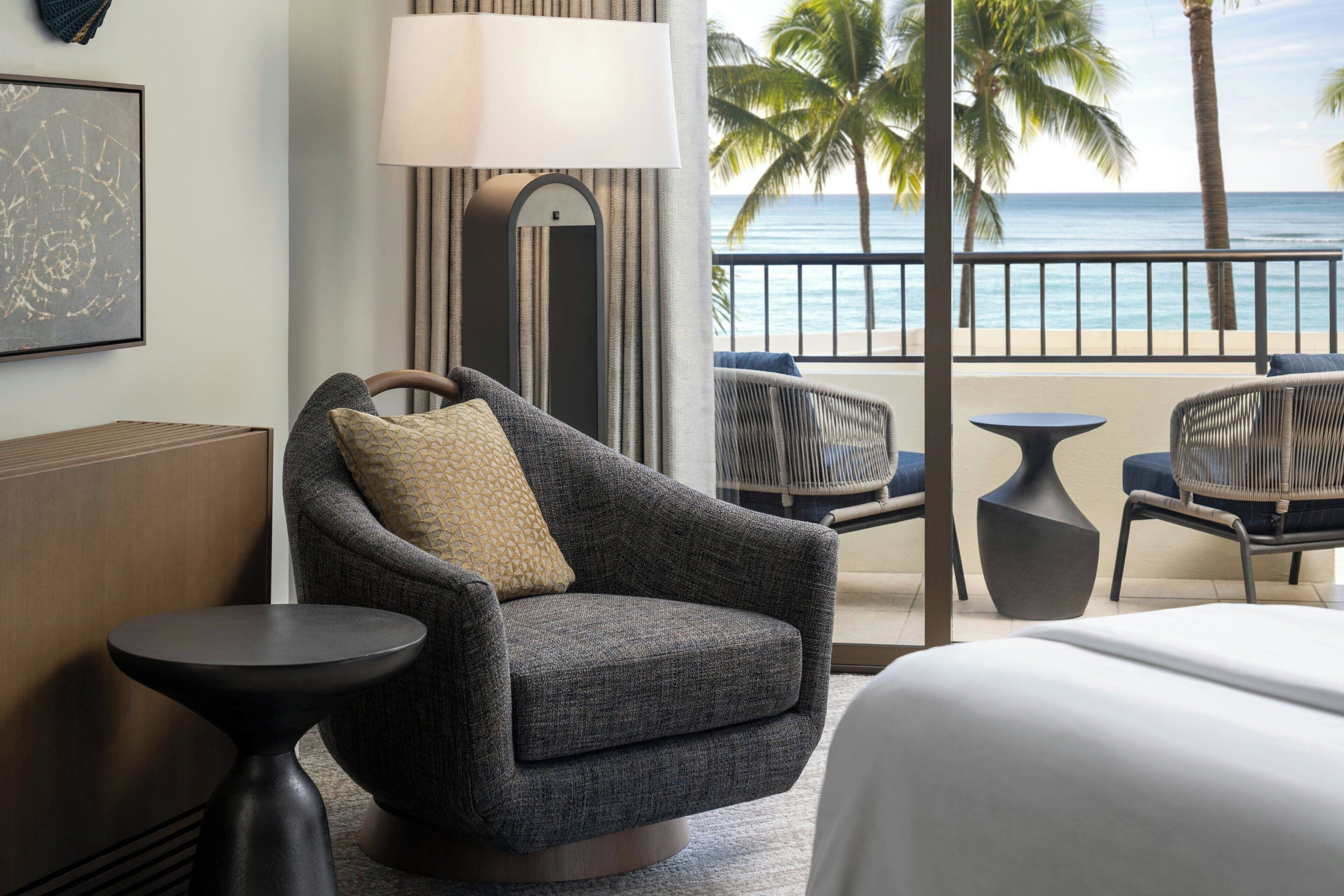 Habitación de hotel con vista al océano, un balcón con mobiliario de mimbre y una cama grande.