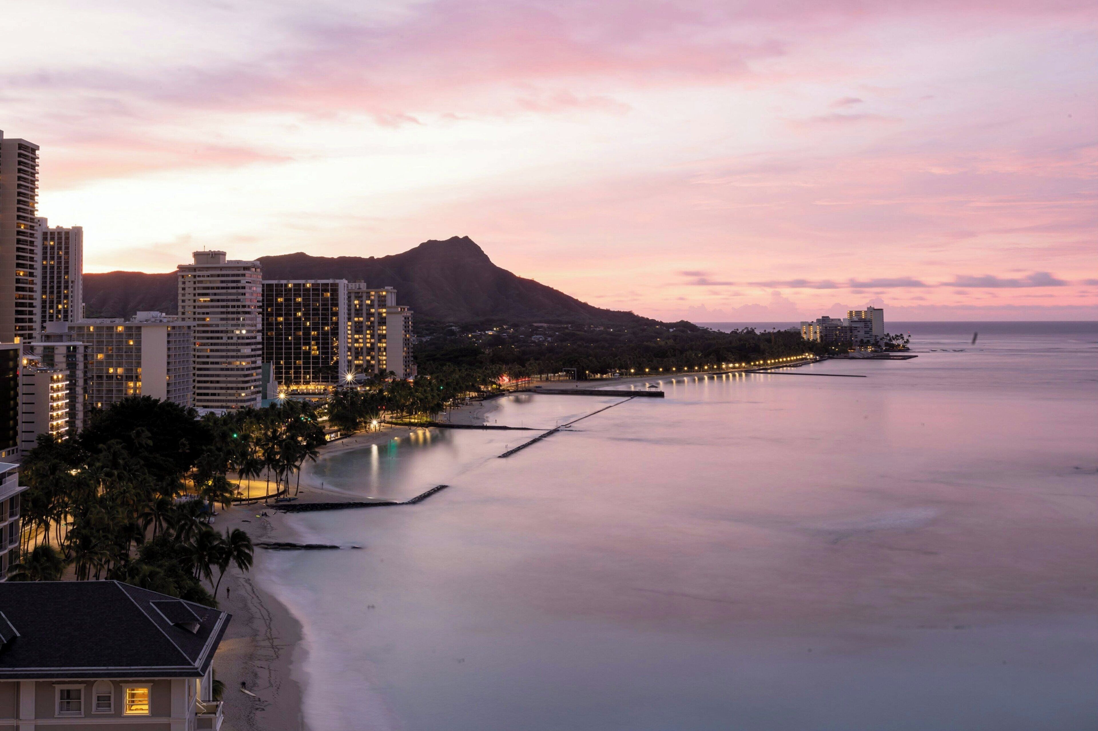 A coastal cityscape with high-rise buildings, a beach, and a mountain in the background.