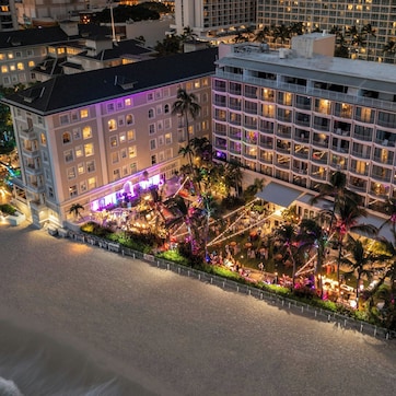 A hotel with multiple floors, a beachfront location, and a well-lit outdoor area with palm trees.