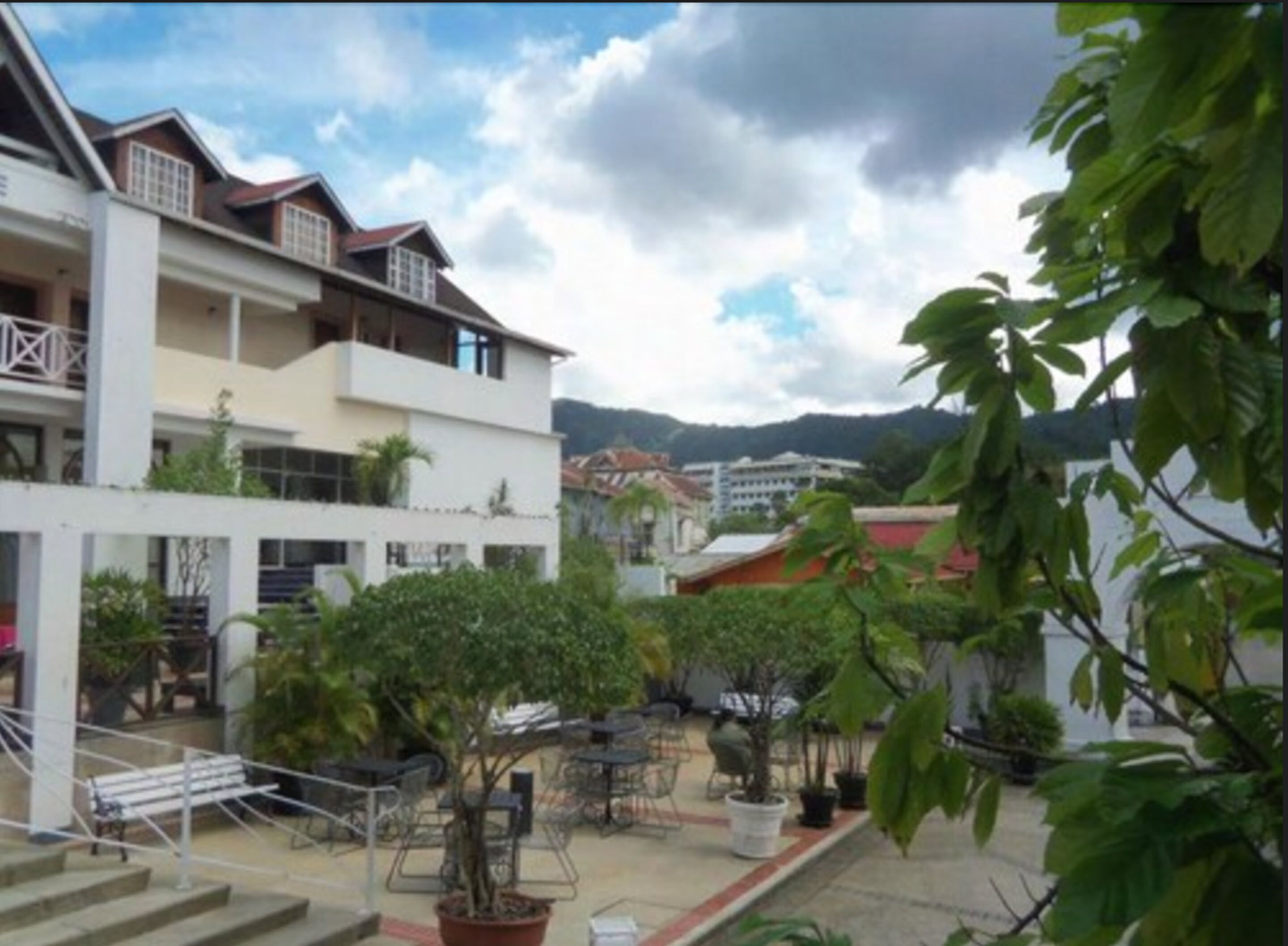 A courtyard with outdoor seating, steps leading to a building, and a view of surrounding buildings and mountains.