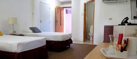 Habitación de hotel con dos camas, un escritorio con un atril de bolígrafos, una lámpara y un equipo de aire acondicionado.