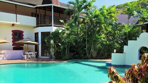 A pool area with a clear blue pool, surrounded by lush greenery and a two-story building with balconies. - The Normandie Hotel (Port of Spain)