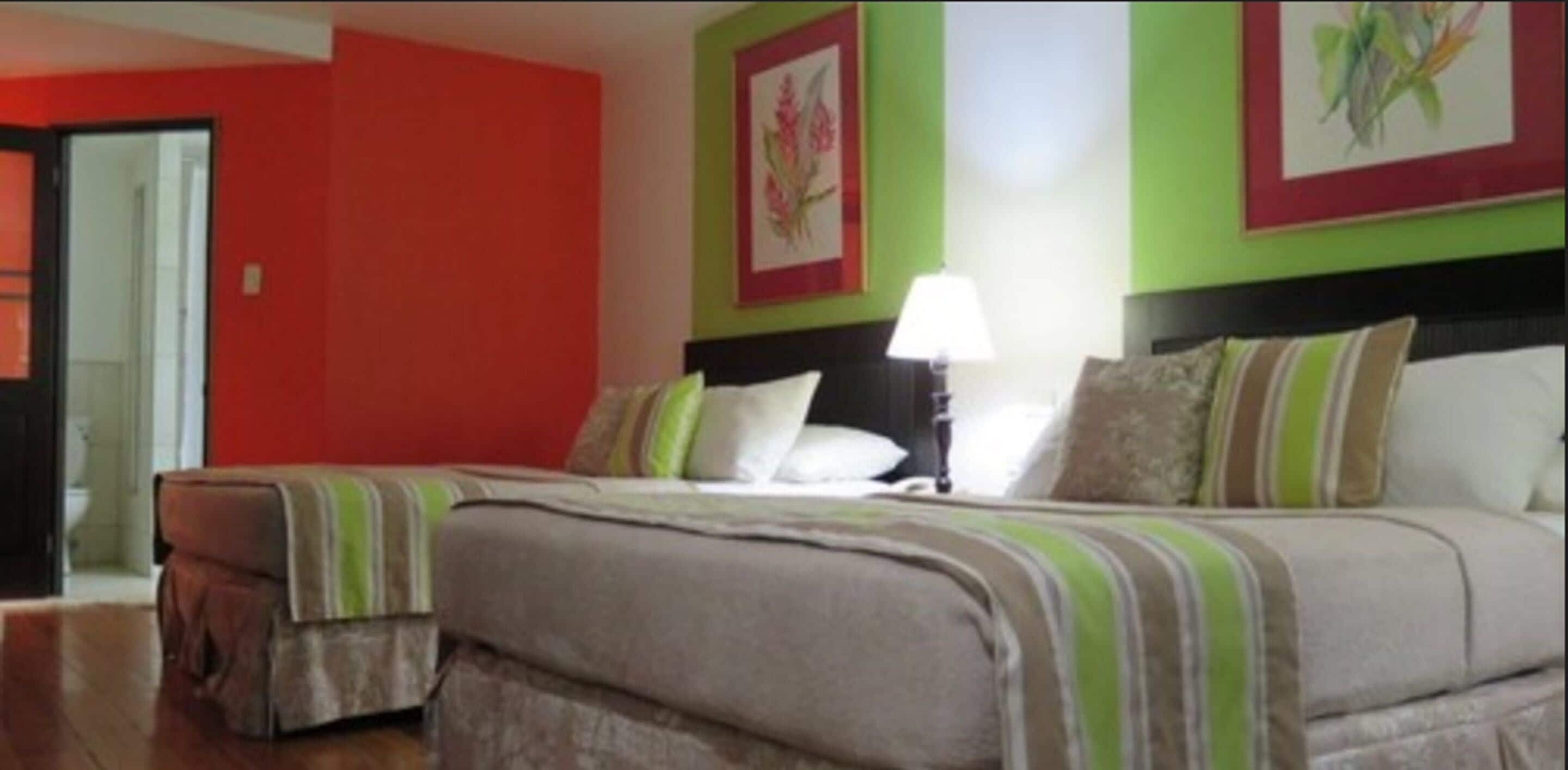 A hotel room with two beds, a green and red color scheme, and a framed floral artwork on the wall.