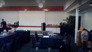 A conference room with tables set for a meeting, a podium, and a person standing at the front. - The Normandie Hotel (Port of Spain)