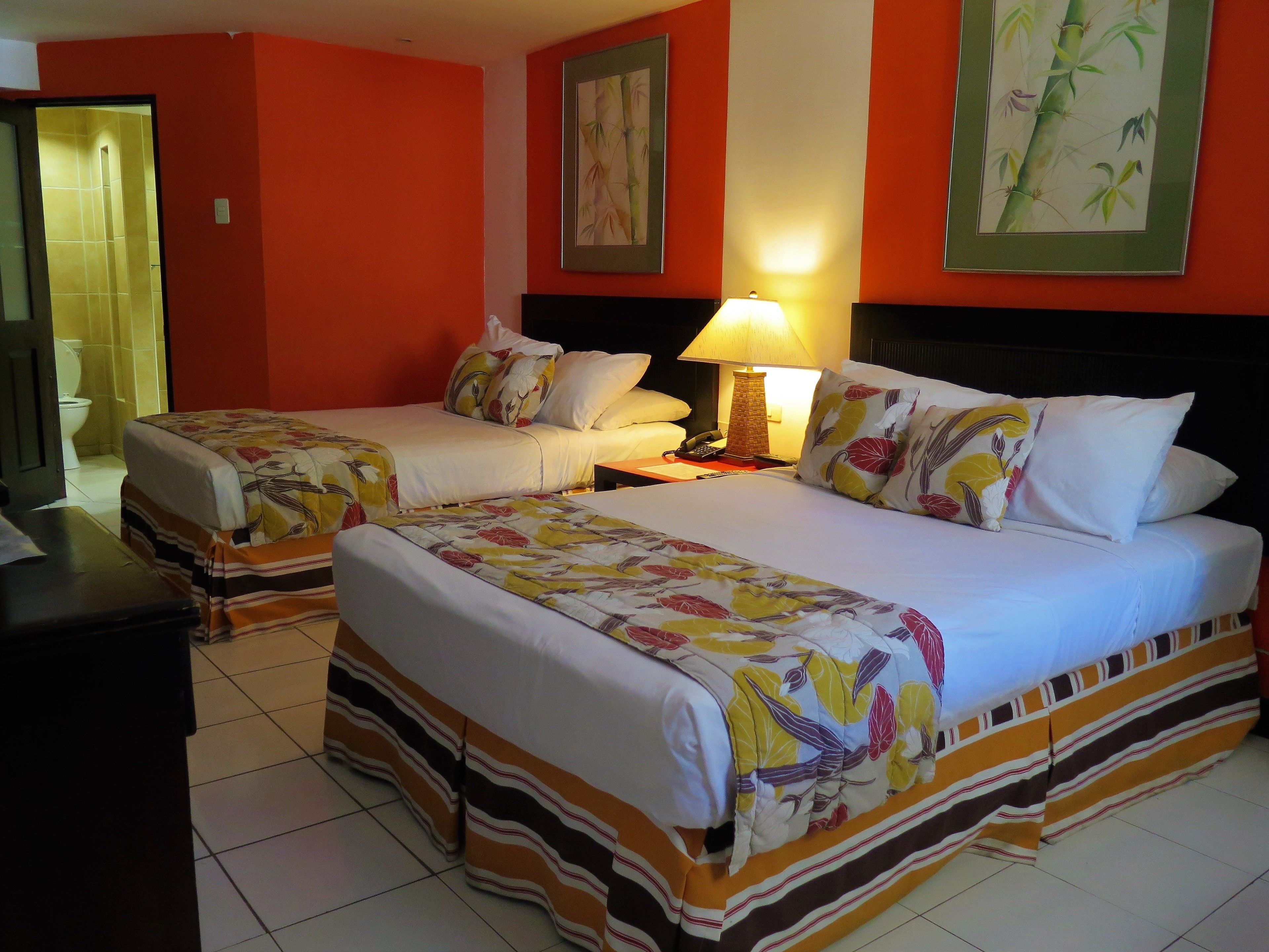 A hotel room with two beds, a bathroom, and a nightstand with a lamp.