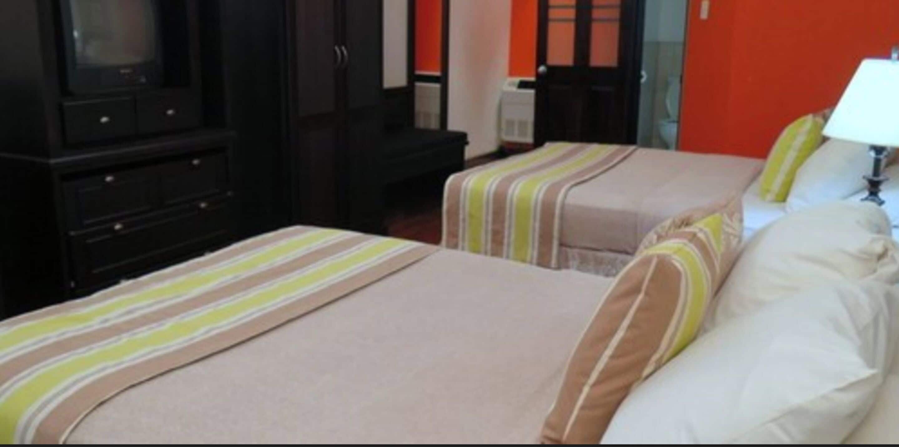 Une chambre d’hôtel avec deux lits, une télévision, un bureau et un mur rouge.