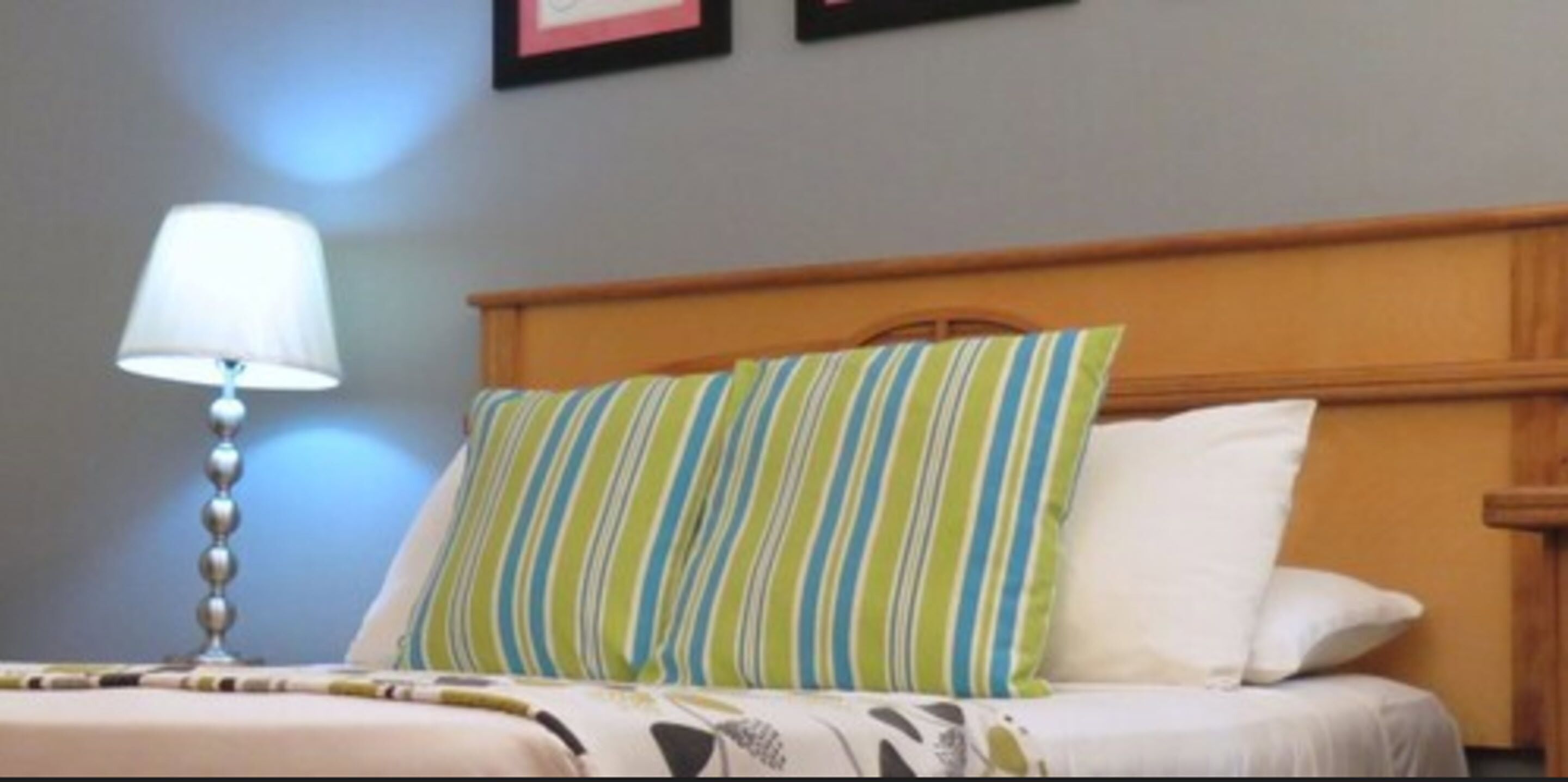A neatly made bed with striped pillows, a bedside lamp, and a framed picture on the wall.