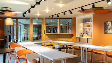 A modern dining area with long tables, orange chairs, and pendant lighting.