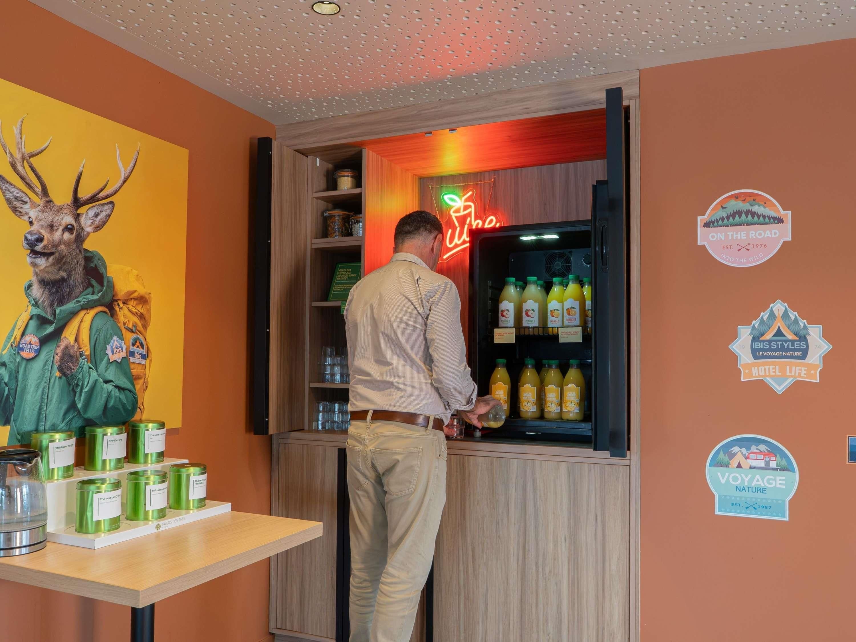 Un hombre en un bar con un letrero de neón, un refrigerador lleno de bebidas y una pared con diversos adhesivos.