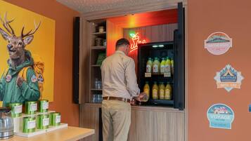 Un hombre en un bar con un letrero de neón, un refrigerador lleno de bebidas y una pared con diversos adhesivos.
