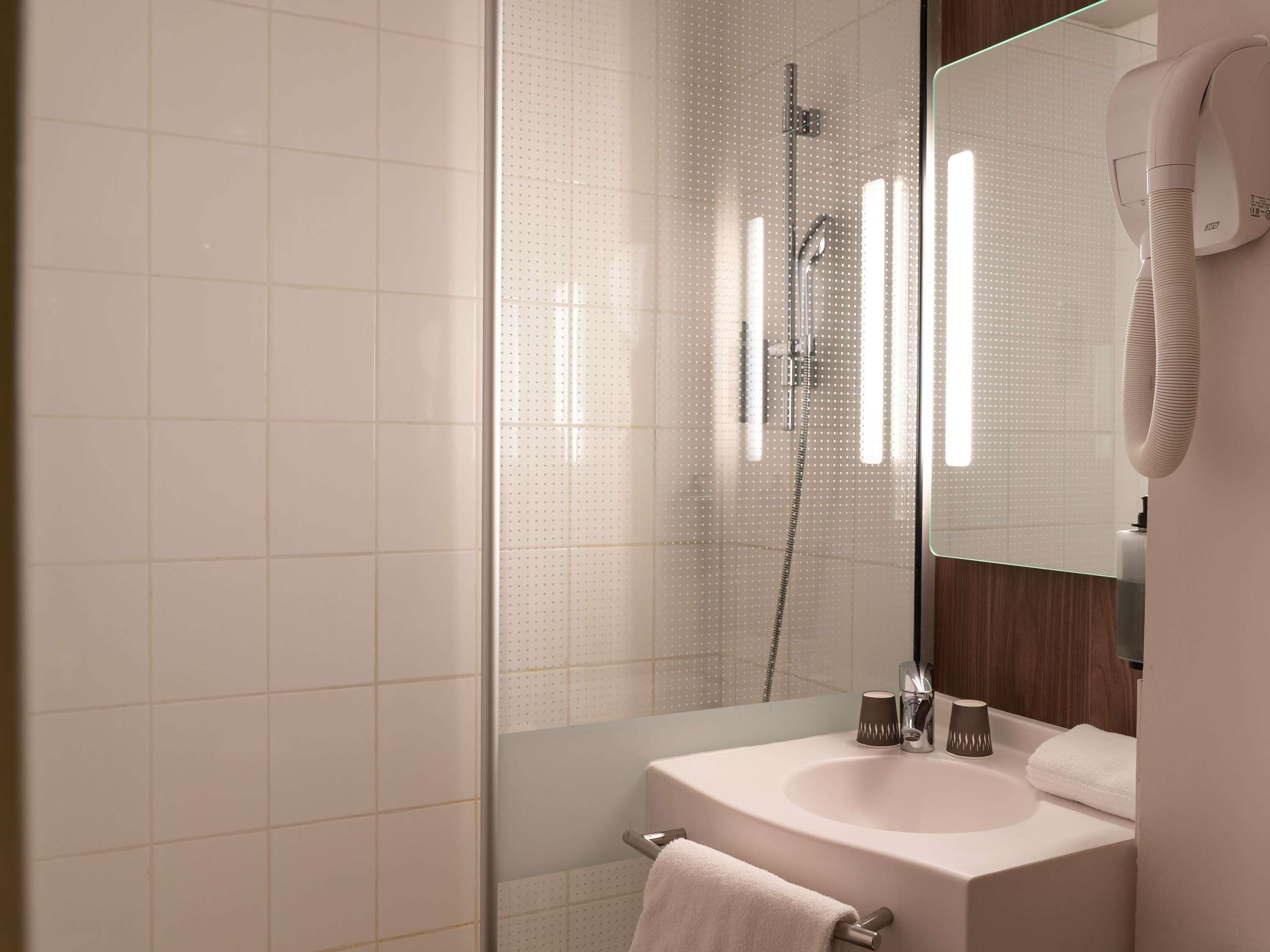 A modern bathroom with a glass shower enclosure, a sink with a mirror, and a hairdryer mounted on the wall.