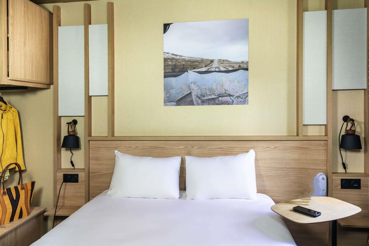 Une chambre d’hôtel avec un lit, une carte accrochée au mur, une lampe et un porte-manteau.