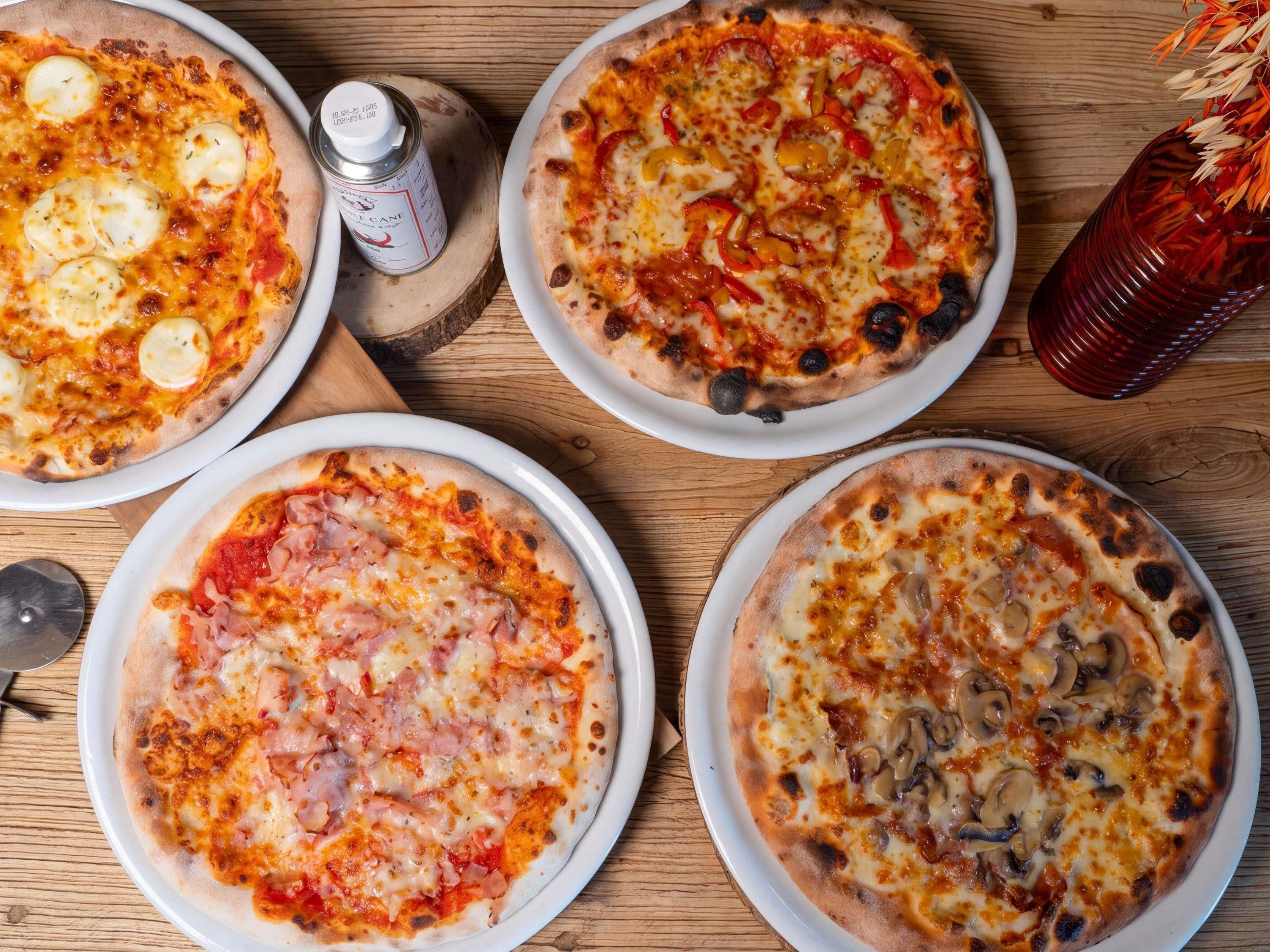 Four pizzas on plates with a wooden table and a bottle of sauce.