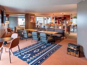 A modern cafe with tables and chairs, a patterned rug, and a counter with kitchen items. - Ibis Styles Rouen Parc Expo Zenith (Saint-Etienne-du-Rouvray)