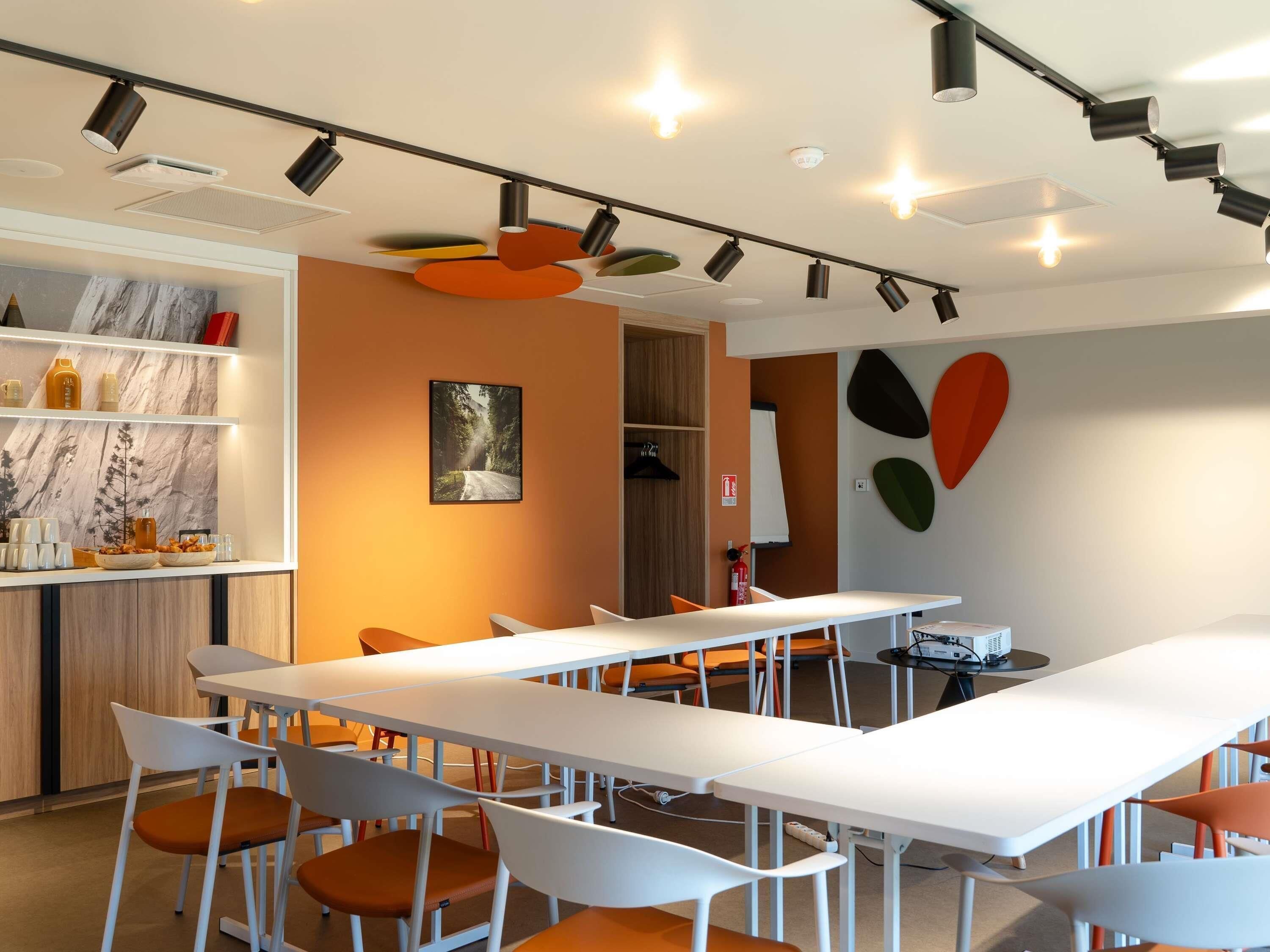 A modern conference room with white tables and chairs, a whiteboard, and a painting on the wall.