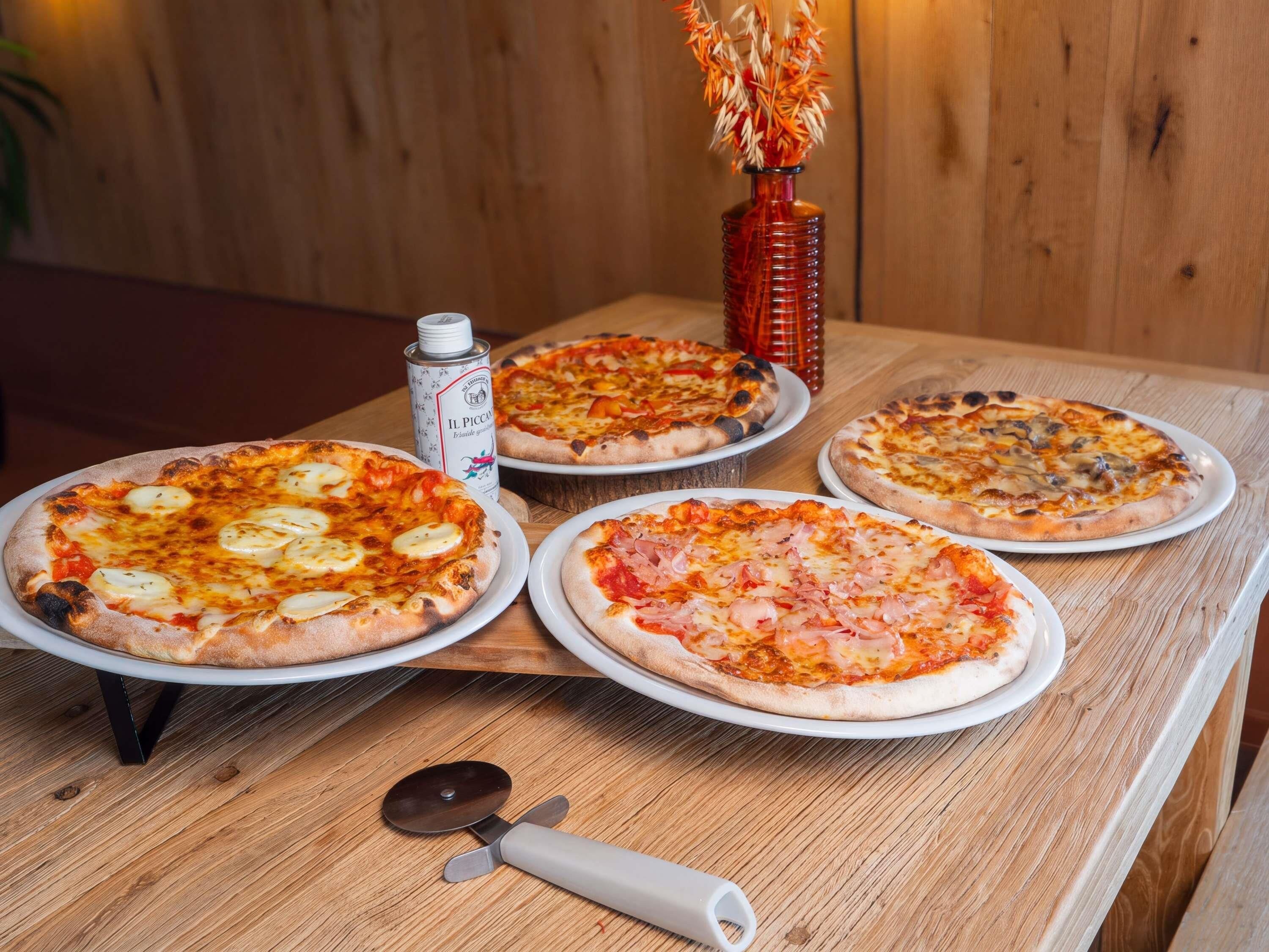 Four pizzas on a wooden table with a pizza cutter and a can of beer.