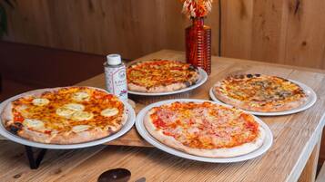Quatro pizzas sobre uma mesa de madeira, com um cortador de pizza e uma lata de cerveja.